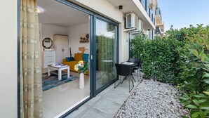 A modern apartment with a sliding glass door leading to a living area, a small patio with a table and chairs, and a well-maintained garden. - Holiday apartment with air conditioning and Wi-Fi (Poreč)
