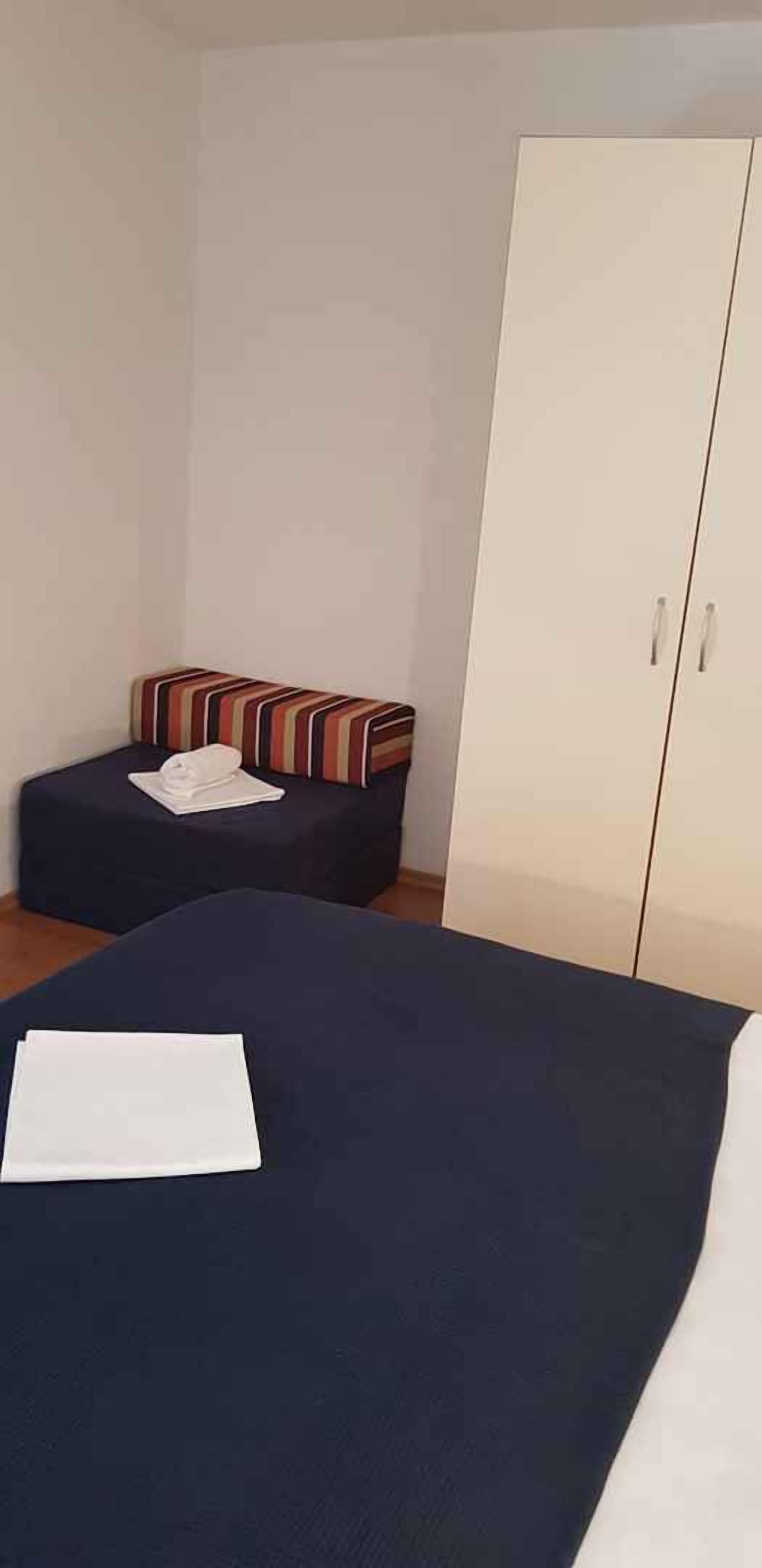 Un dormitorio con cama, una pequeña zona de estar con cojín a rayas y un armario.