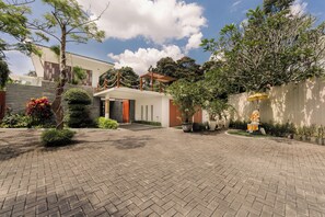 A modern building with a paved courtyard, surrounded by greenery and a decorative fence. - The Muse Luxury Eco-Living (Tabanan)