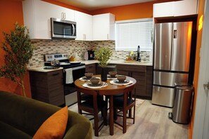 Una cocina moderna con armarios blancos, un refrigerador de acero inoxidable, un microondas y una mesa de comedor con tazones y platos.
