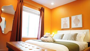 A bedroom with a large bed, a bench, a window with curtains, and two framed pictures on the wall. - The Tangerine Retreat - Retro Dallas Downtown Vibe (Dallas)