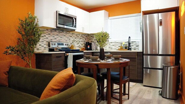 A modern kitchen with white cabinets, a stainless steel refrigerator, and a dining area with a table and chairs. - The Tangerine Retreat - Retro Dallas Downtown Vibe (Dallas)