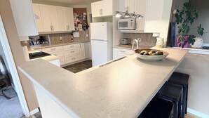Een moderne keuken met witte kasten, een centraal eiland met krukken, een magnetron en een koelkast.