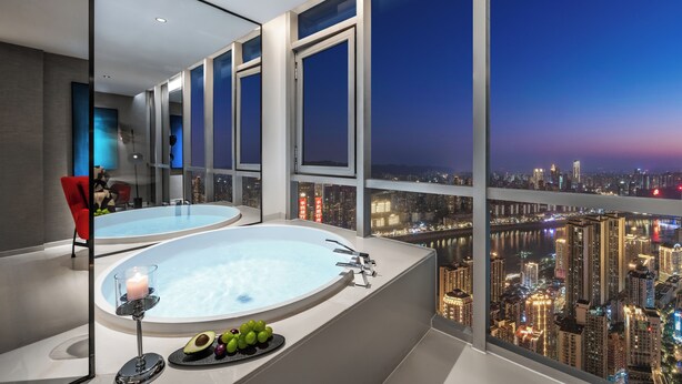 A modern bathroom with a bathtub, a glass table with fruits, and a view of a cityscape at dusk. - SEYA Panoramic Hotel - Chongqing Cloud Eye - Managed by SEYA GROUP (Chongqing)