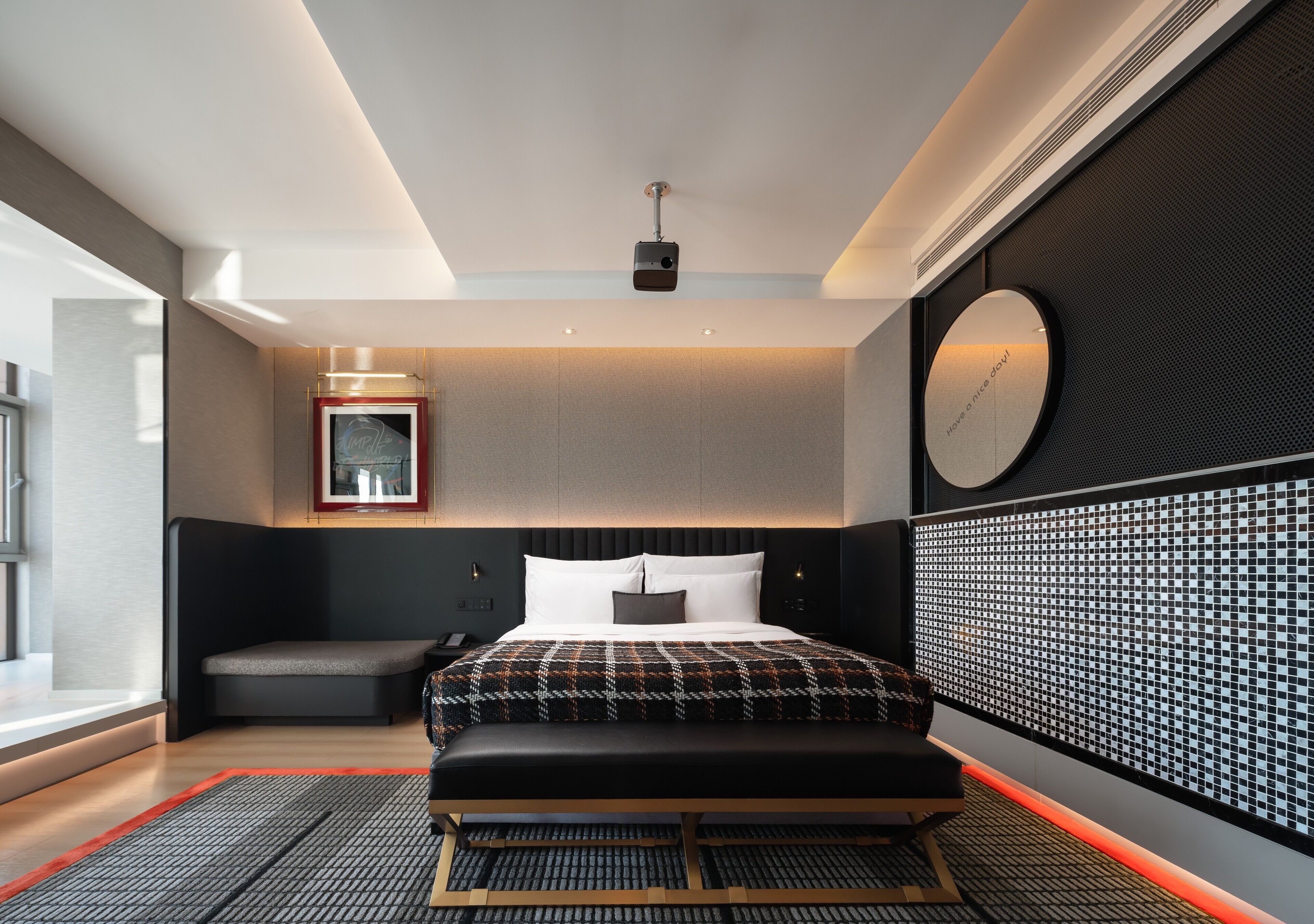 Moderni hotellihuone, jossa on suuri sänky, yöpöytä, seinäkello ja kuvioitu seinä.