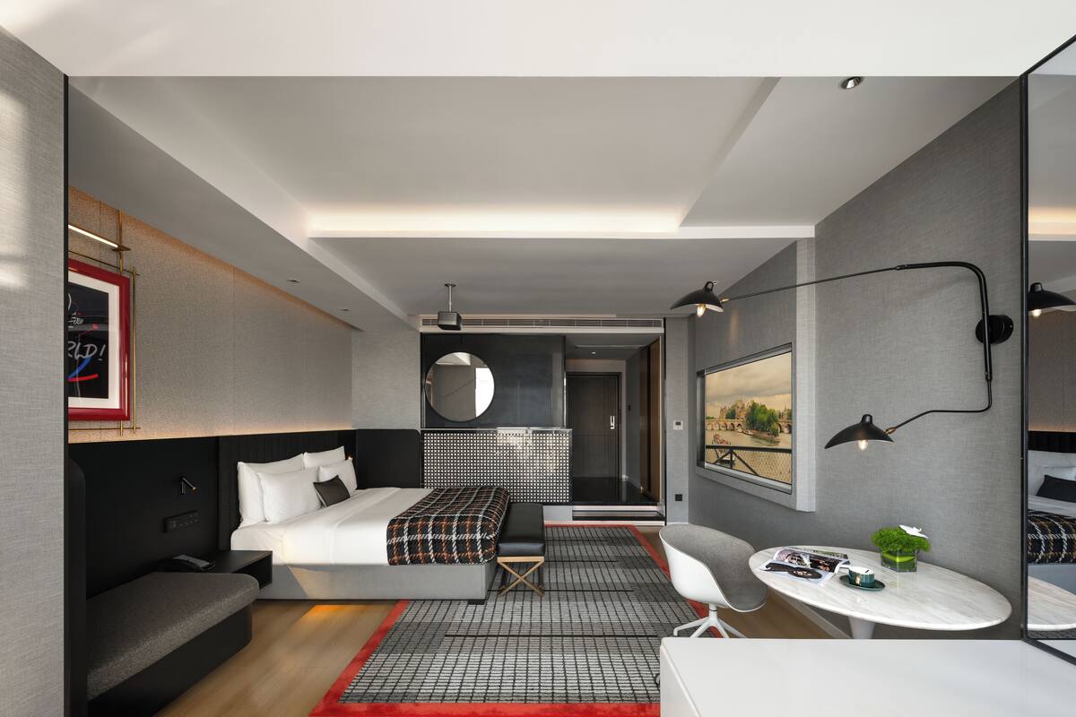 Une chambre d’hôtel moderne équipée d’un lit, d’une table de chevet, d’une chaise et d’une petite table agrémentée d’une plante.