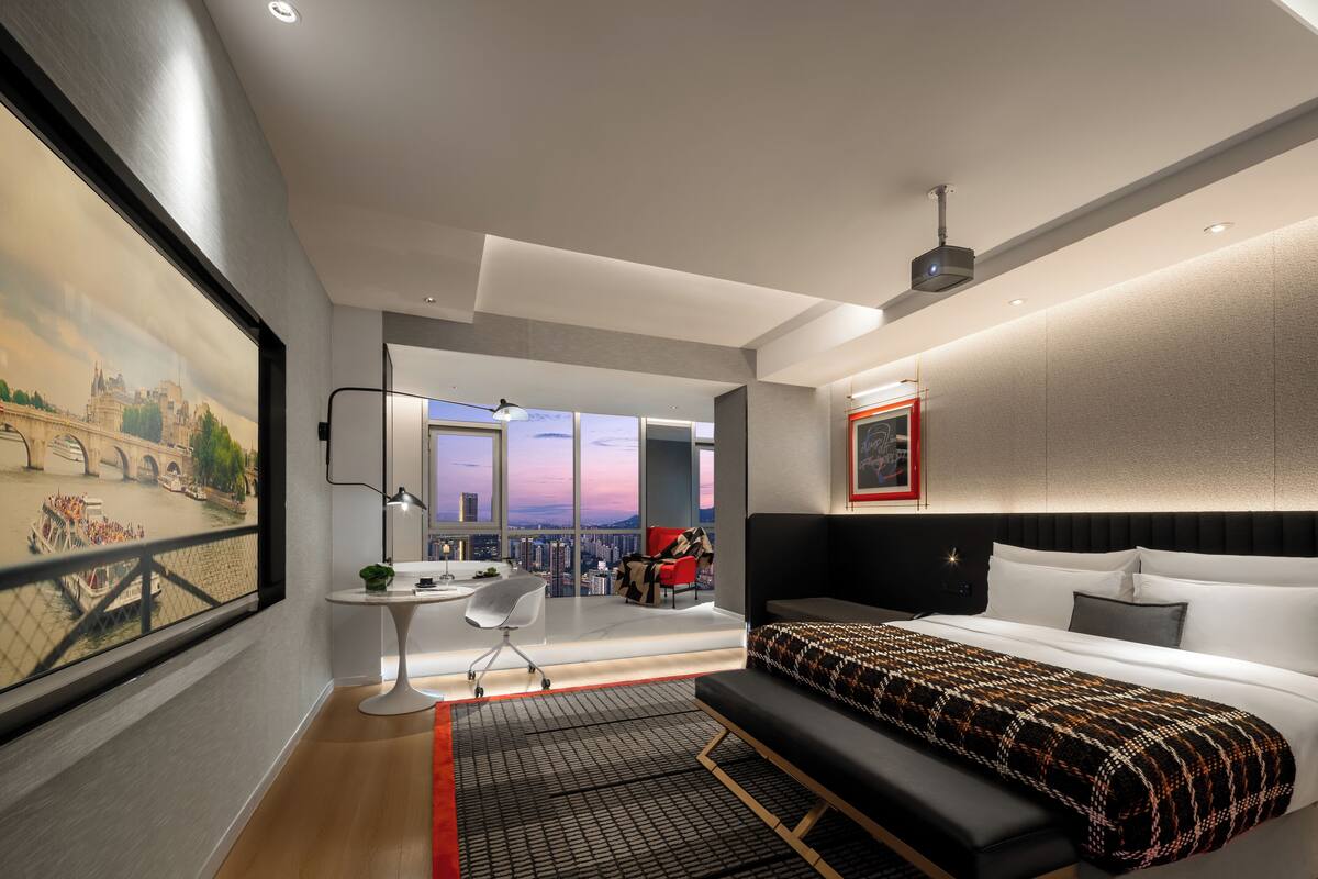 Une chambre d’hôtel moderne, dotée d’un grand lit, d’un bureau et offrant une vue sur le paysage urbain grâce à une grande fenêtre.