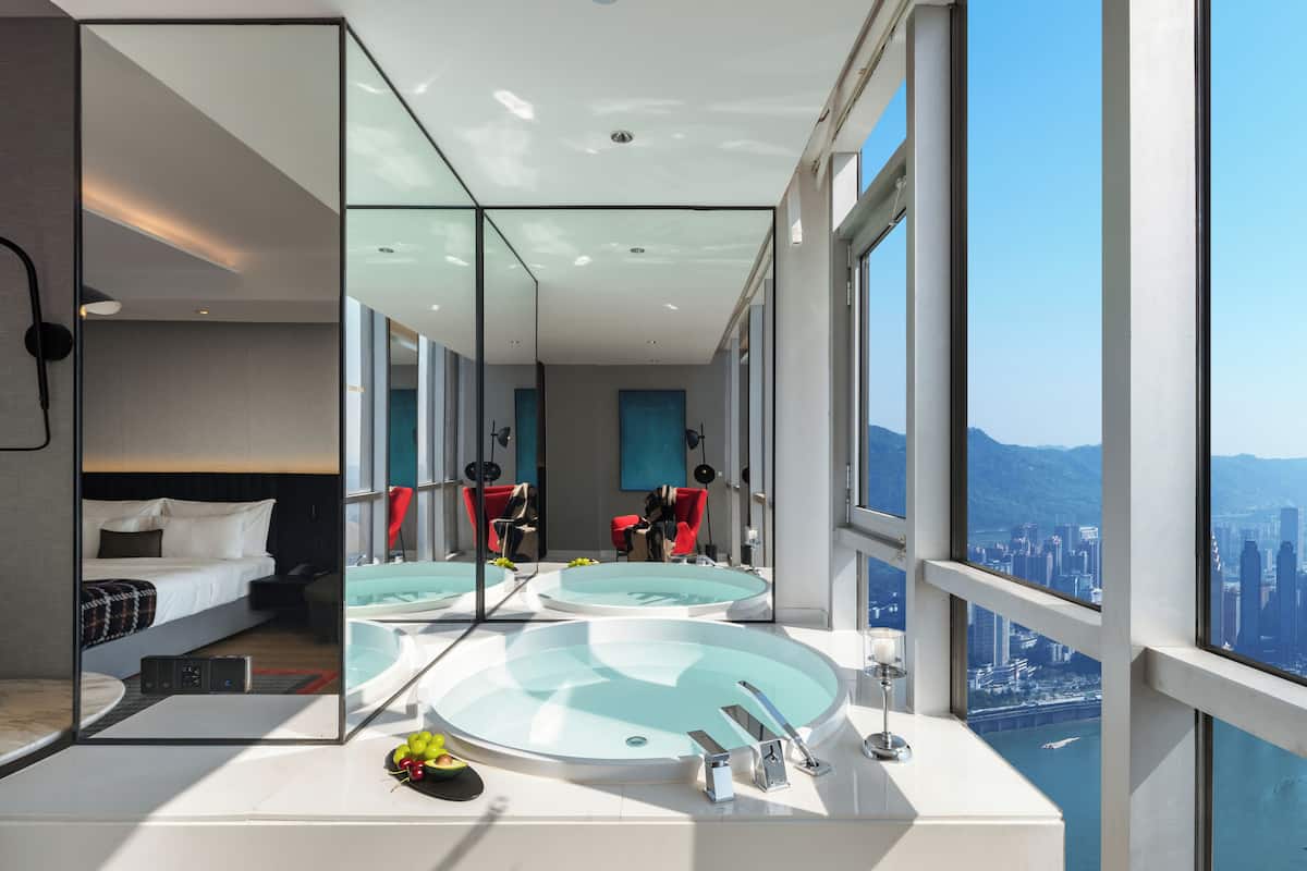 Una habitación de hotel moderna con un espejo grande, una bañera redonda y vistas a la ciudad.