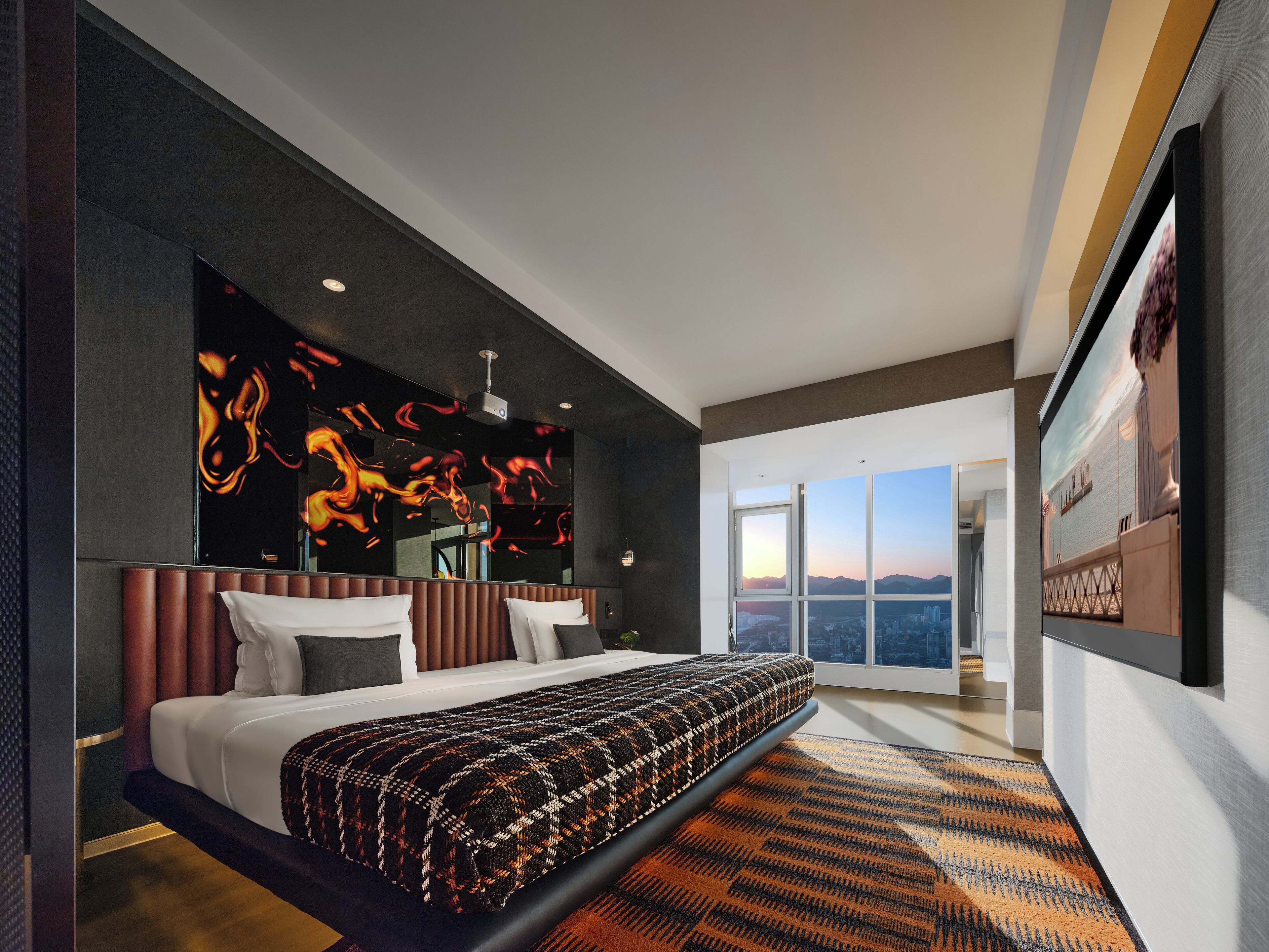 A modern hotel room with a large bed, a city view, and a unique wall art piece.