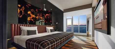 A modern hotel room with a large bed, a city view, and a unique wall art piece.
