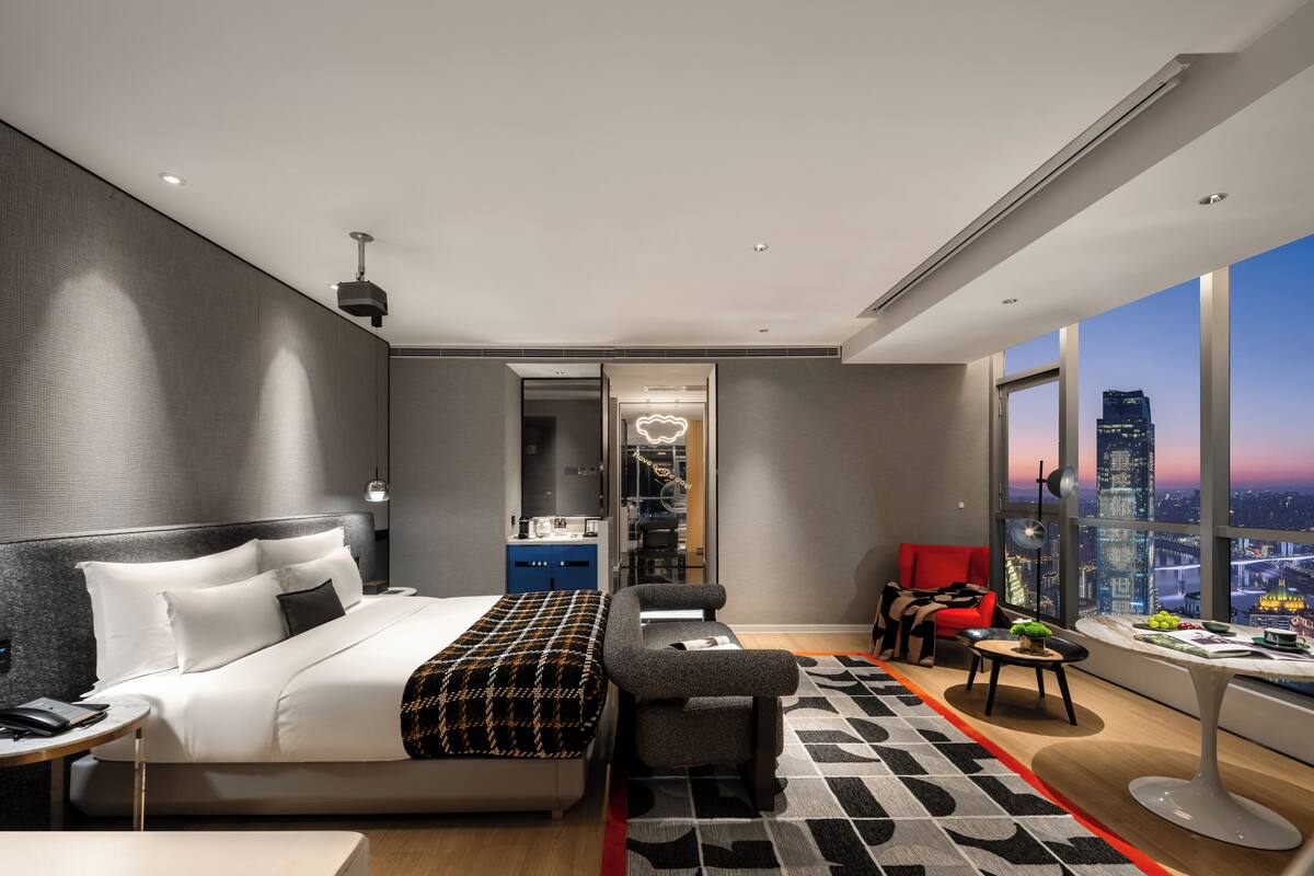 Une chambre d’hôtel moderne, dotée d’un grand lit, d’un bureau, d’une chaise et offrant une vue sur le paysage urbain.