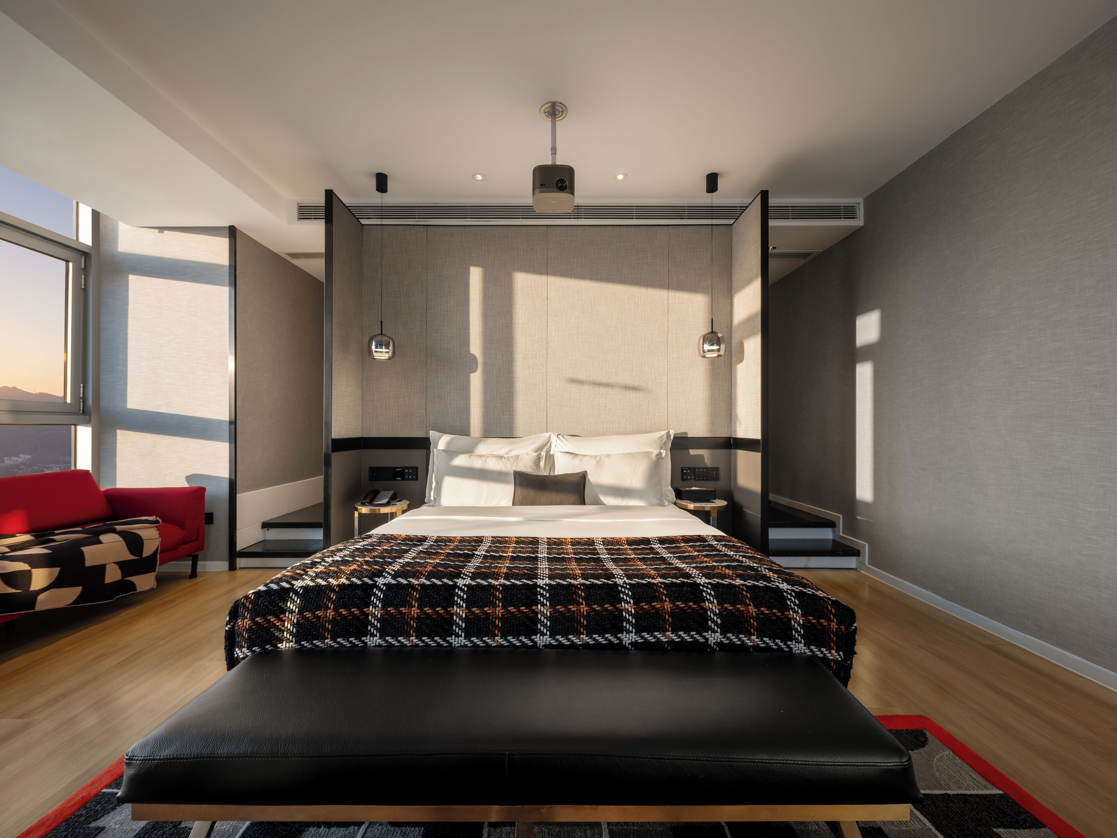 Ein modernes Hotelzimmer mit einem großen Bett, einem roten Sofa, einer Bank und Blick auf die Stadt.
