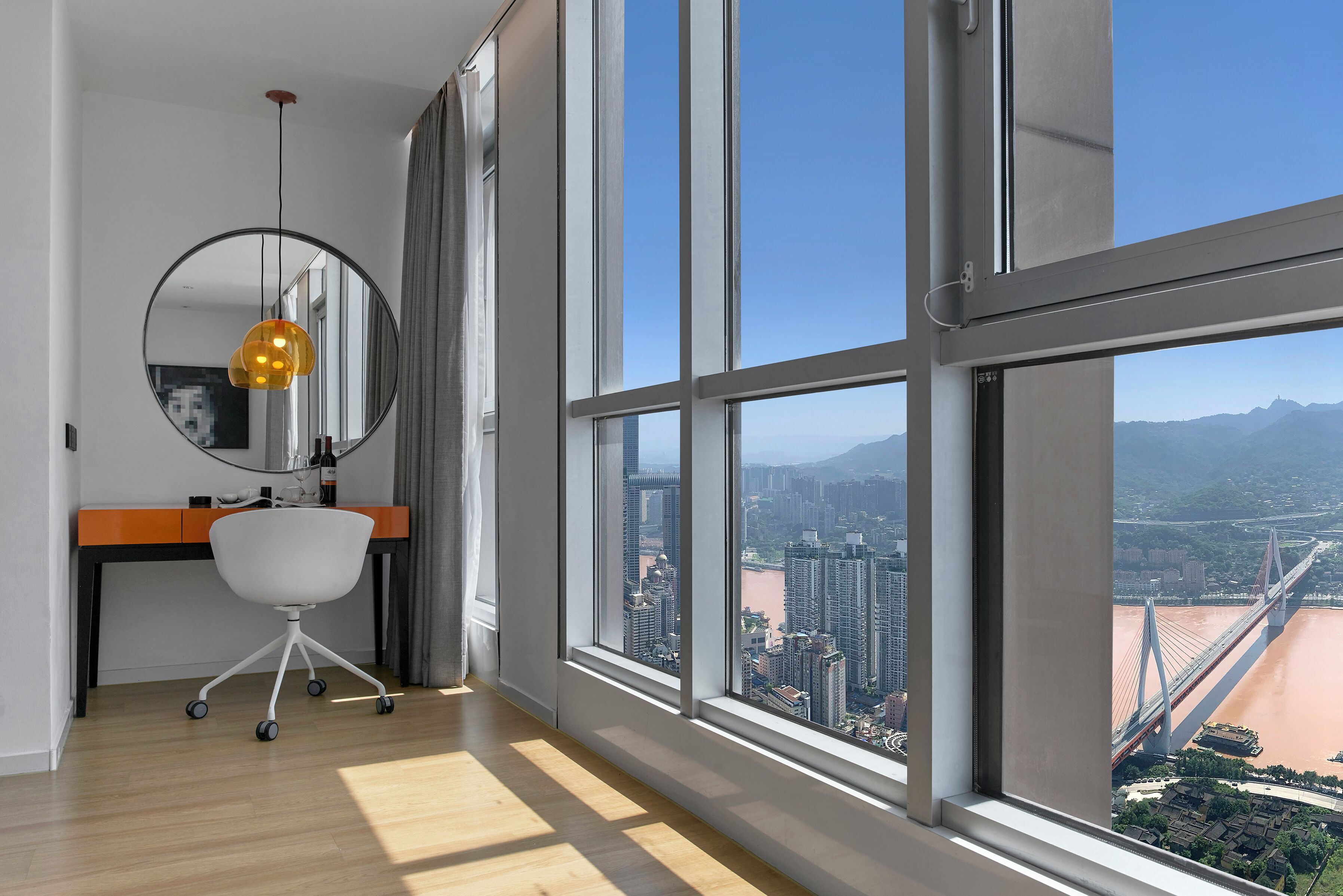 Una habitación moderna con un ventanal grande, un escritorio, una silla y una lámpara colgante.
