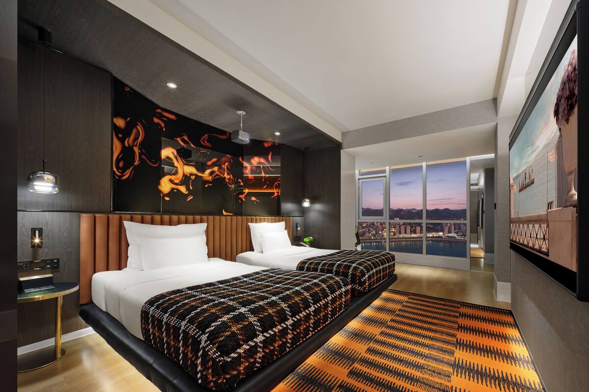 Une chambre d’hôtel moderne dotée d’un grand lit, offrant une vue sur le paysage urbain et agrémentée d’une œuvre d’art murale originale.