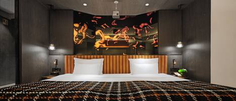 A modern hotel room with a large bed, a headboard with vertical slats, recessed ceiling lights, and a wall-mounted projector.