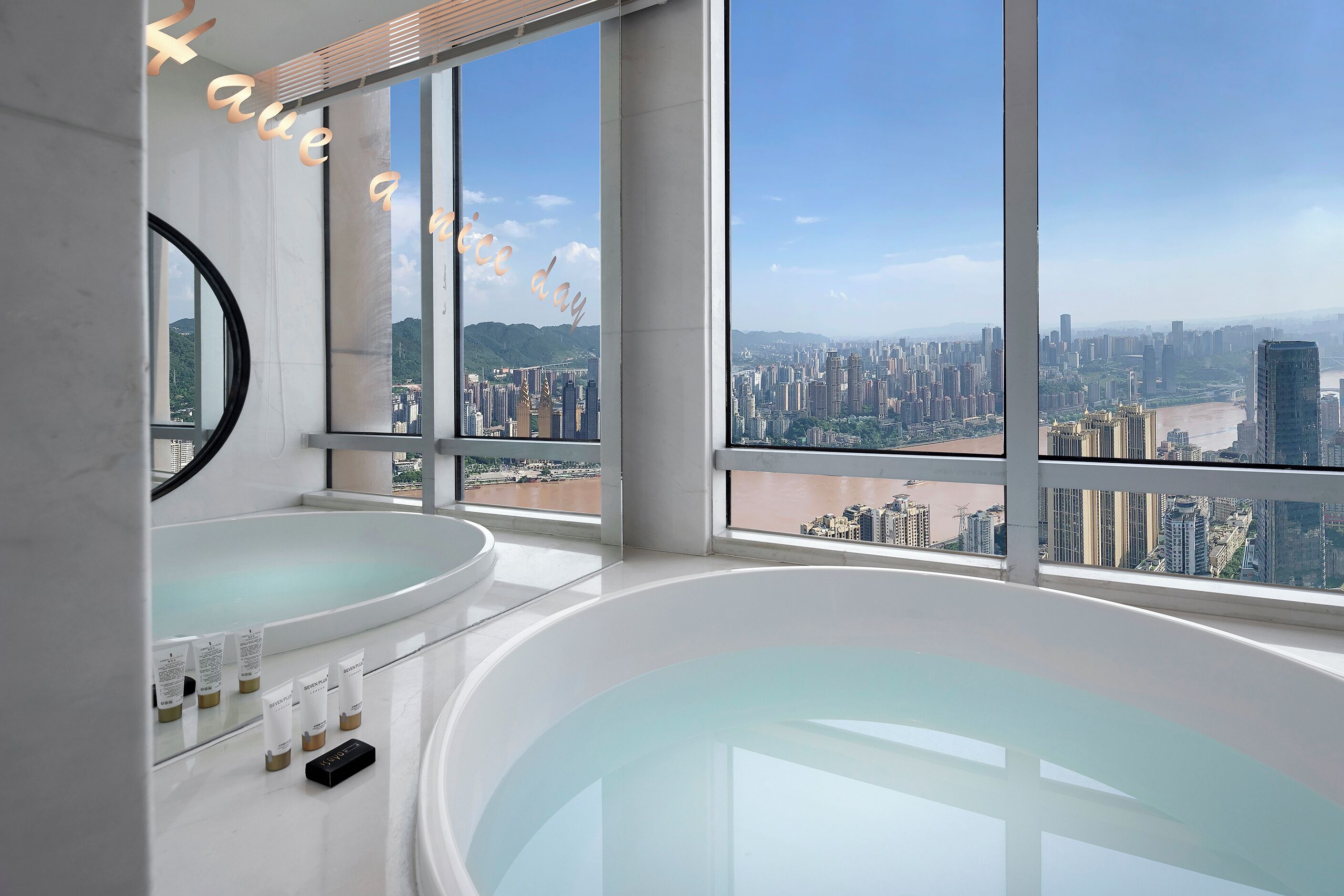 Un baño moderno con una bañera grande, un espejo y vistas de la ciudad a través de amplias ventanas.