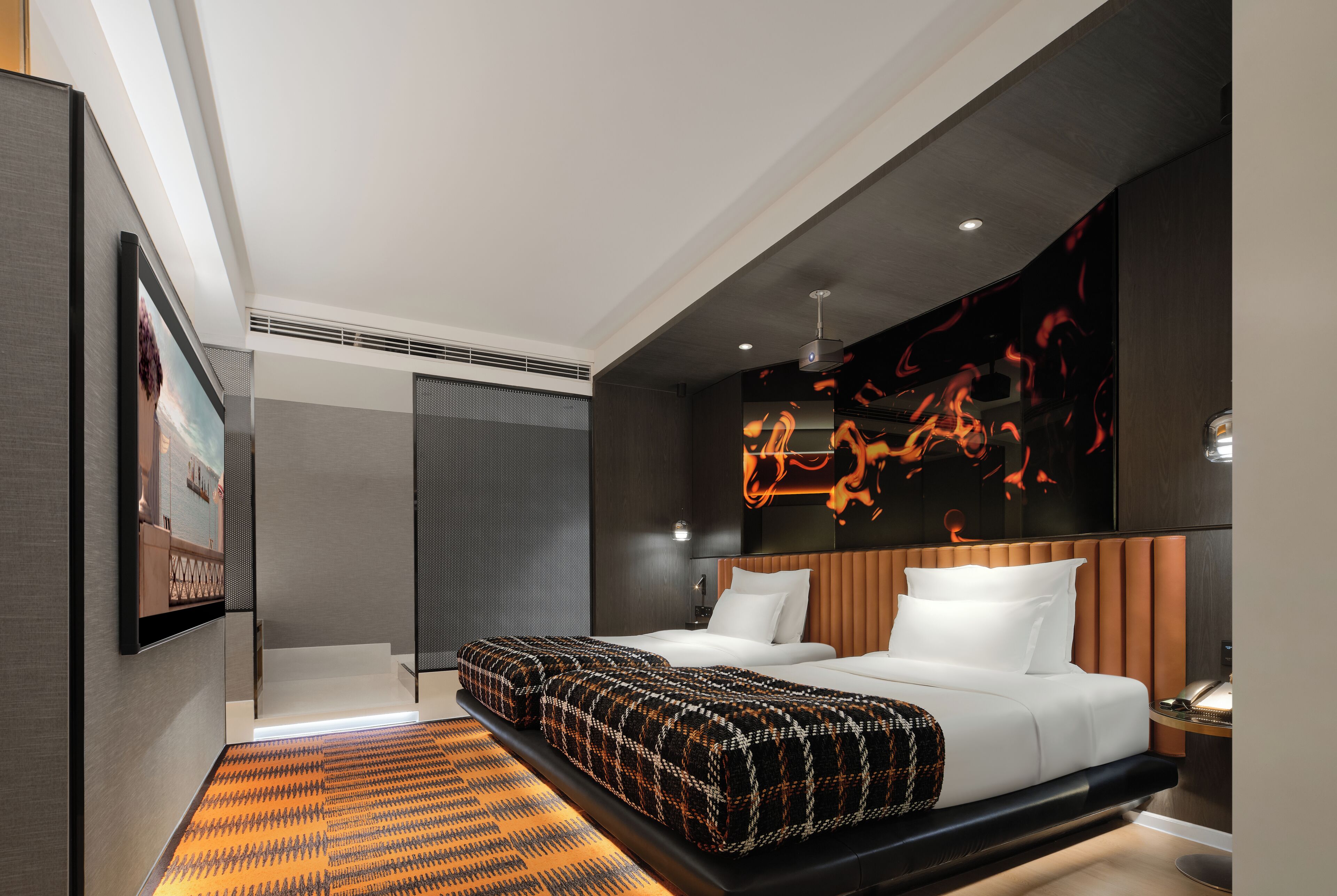 A modern hotel room with a large bed, a seating area, a wall-mounted TV, and a unique light installation.