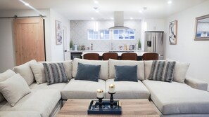 Un salon moderne avec un canapé d’angle, une table basse ornée de bougies et une cuisine en arrière-plan.