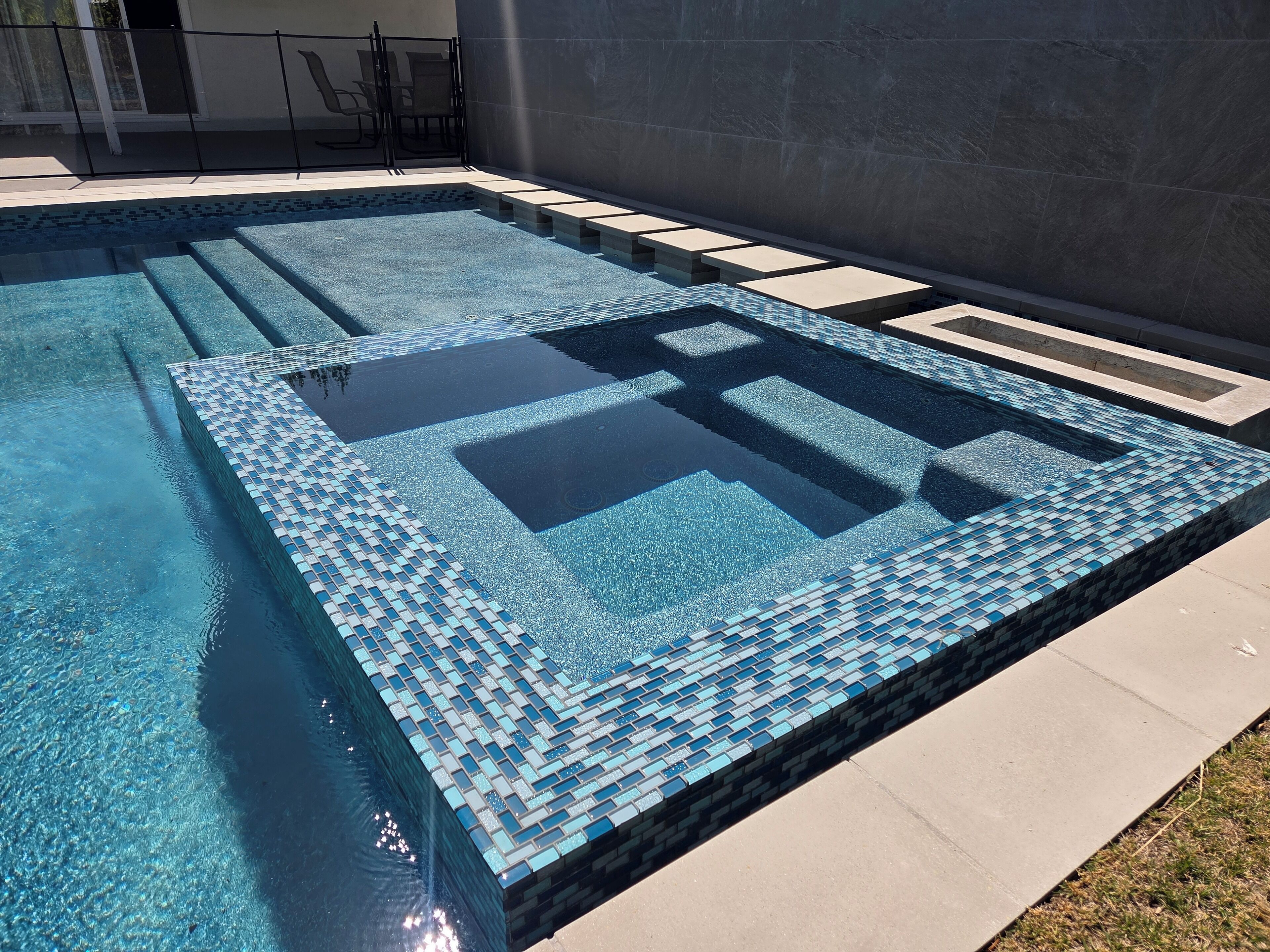 Ein rechteckiger Pool mit einer gefliesten Liegefläche und einem geometrischen Muster auf dem Boden.