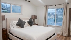 Une chambre avec un grand lit, deux tables de chevet, une fenêtre avec des rideaux et une vue sur l’extérieur.