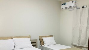 Una habitación de hotel con dos camas, aire acondicionado en el techo y una cortina en la ventana.