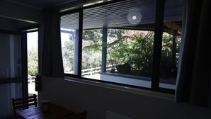A room with a window overlooking a garden, a wooden table, and a chair. - Safe Haven Hillside Retreat (Maungatapere)