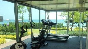 Une salle de sport extérieure abritée, équipée de vélos d’appartement et de tapis de course, offrant une vue panoramique sur la mer et la verdure.