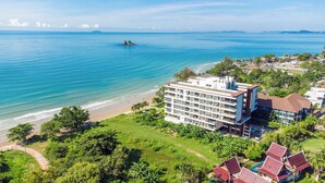 Un hôtel en bord de mer, avec plusieurs étages, une vue sur la plage et une végétation luxuriante.