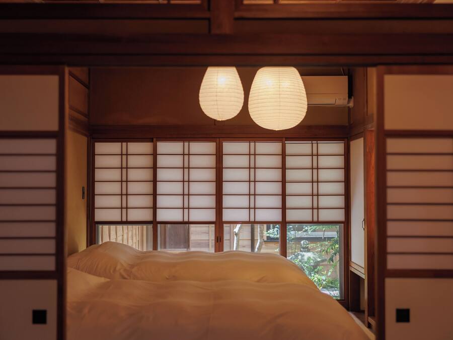 Una tradizionale stanza giapponese con pavimento in tatami, un letto basso, porte scorrevoli shoji e due lanterne di carta.
