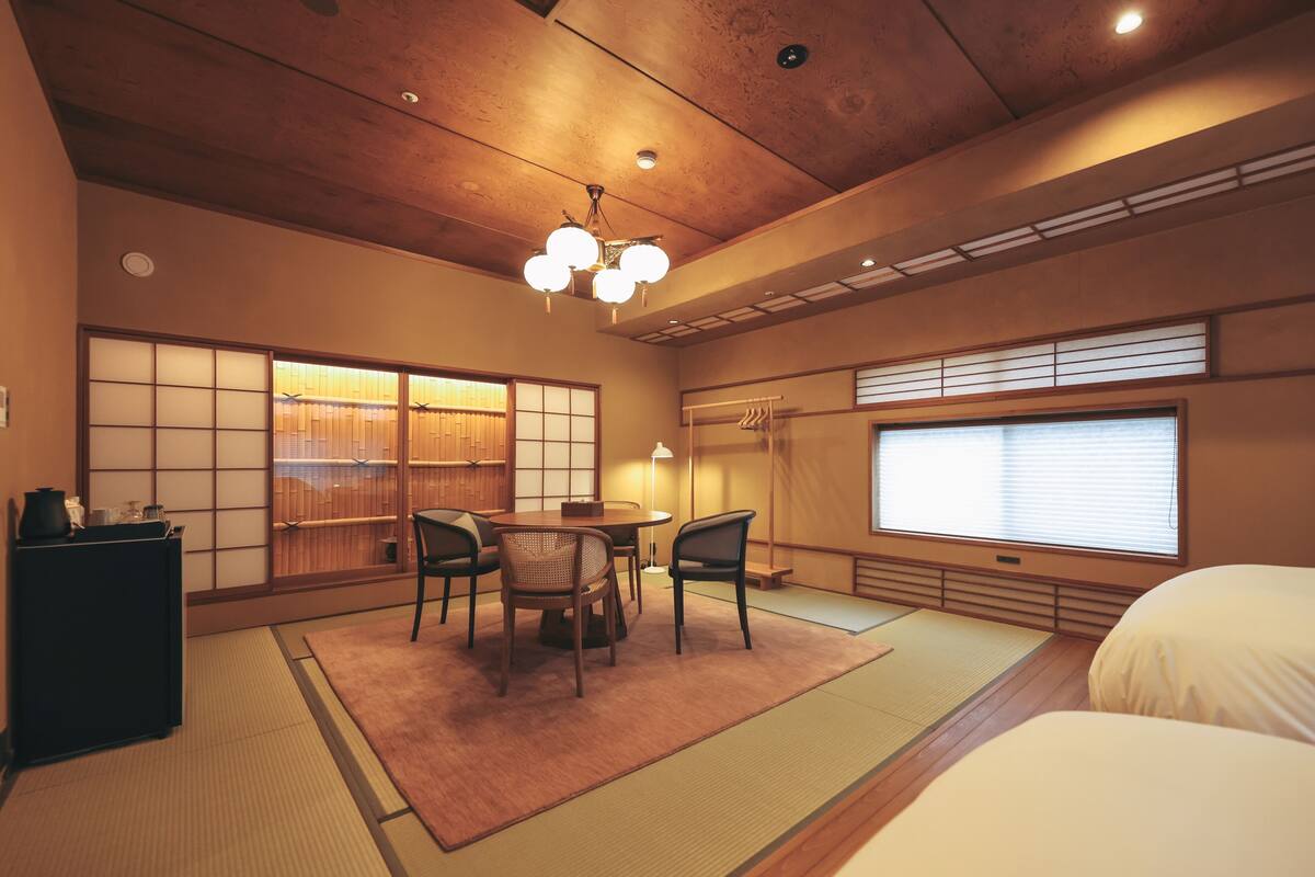 Ein traditioneller japanischer Raum mit Tatami-Böden, einem niedrigen Tisch mit Stühlen, einem Bett und verschiebbaren Shoji-Bildschirmen.