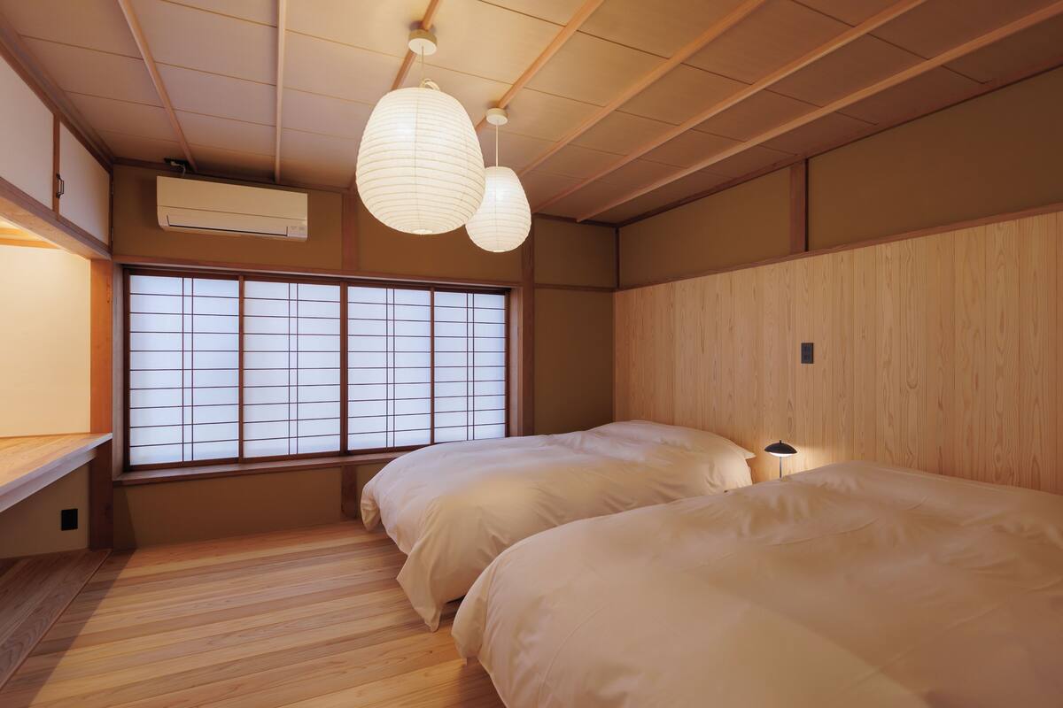 Ein traditioneller japanischer Raum mit Tatami-Boden, einem Shoji-Fenster und zwei Betten mit weißer Bettwäsche.