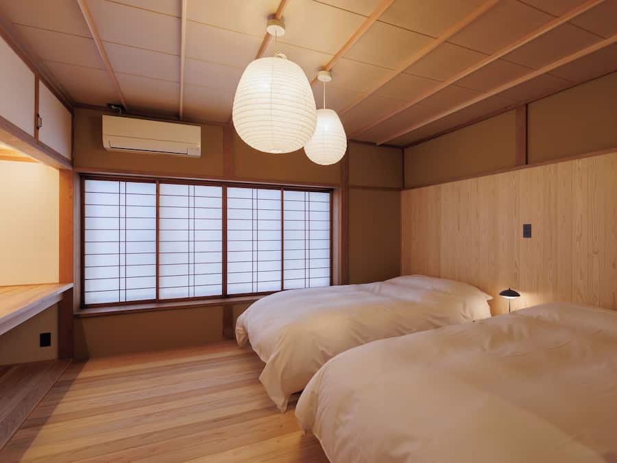 Una habitación japonesa tradicional con suelo de tatami, ventana con celosía de shoji y dos camas con ropa blanca.