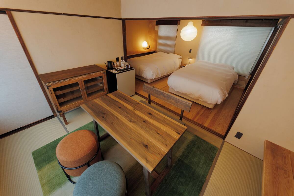 Ein kleines Zimmer mit zwei Betten, einem Schreibtisch, einer Bank und einem Hocker.