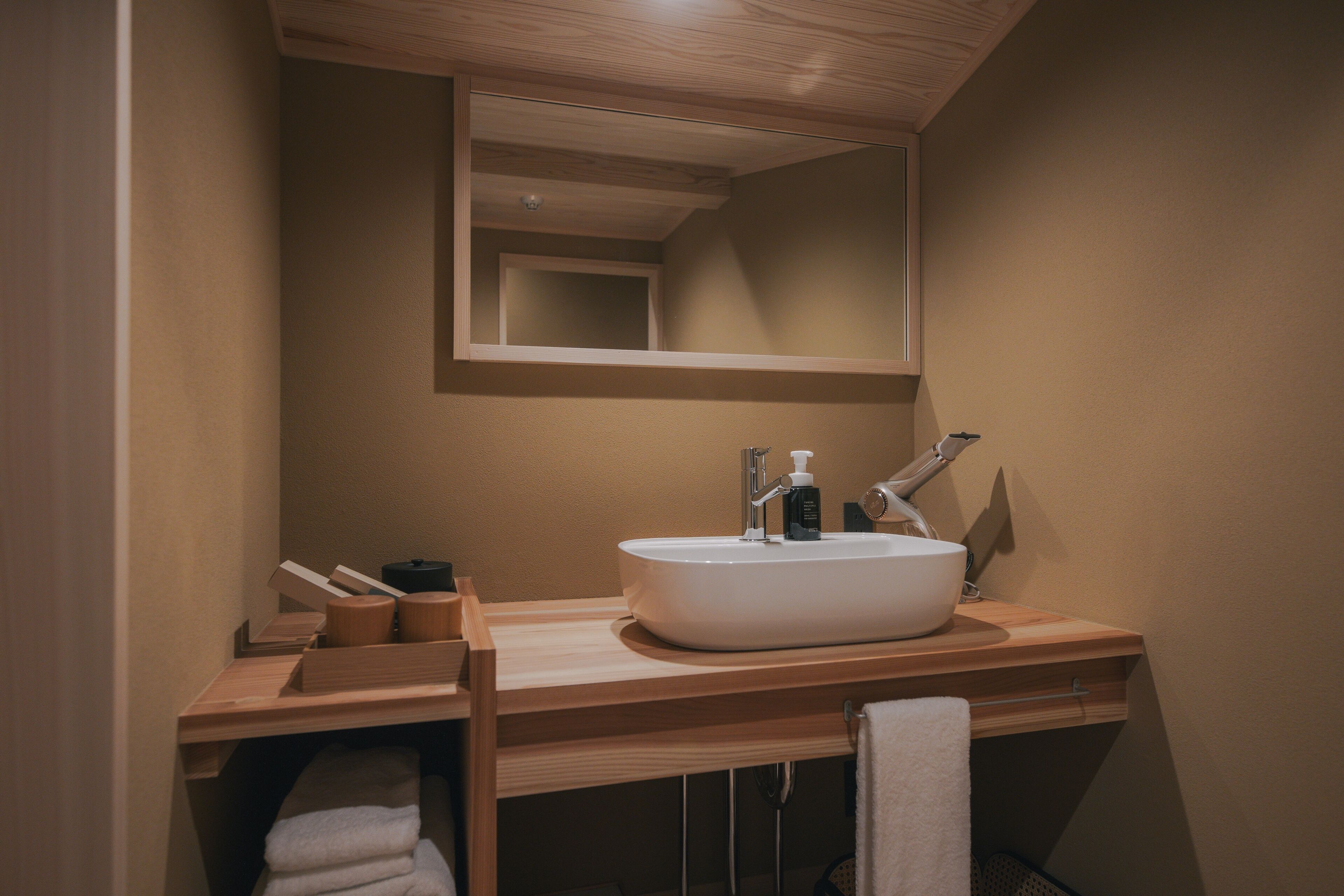 Un baño con tocador de madera, lavamanos blanco, espejo y perchero.