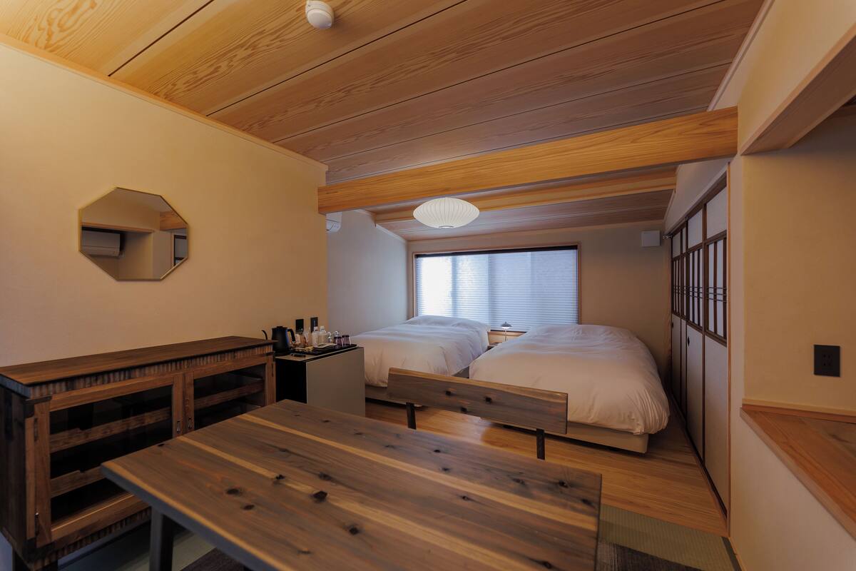 Ein gemütlicher Raum mit zwei Betten, einem Holztisch, einem kleinen Schreibtisch und einem Spiegel an der Wand.