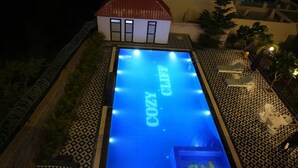 A swimming pool with the words "COZY CLIFF" on the water, surrounded by patterned flooring and a small building in the background. - Cozy Cliff By Marwar Royal – Private Villa with Pool (Barodiya)