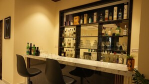 A bar area with a marble countertop, black bar stools, and shelves stocked with liquor bottles and glasses. - Cozy Cliff By Marwar Royal – Private Villa with Pool (Barodiya)