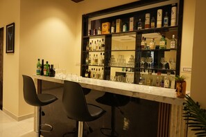 Eine Bar mit Marmorplatte, schwarzen Barhocker und Regalen voller Spirituosen und Gläsern.