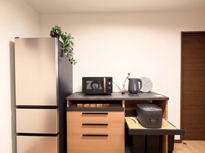 Una cocina compacta con refrigerador, microondas, hervidor de agua y una cafetera pequeña sobre una encimera de madera.
