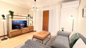 Una sala de estar moderna con un televisor de pantalla plana, un mueble de televisión de madera, un sofá gris, una mesa de centro y una lámpara de pie.