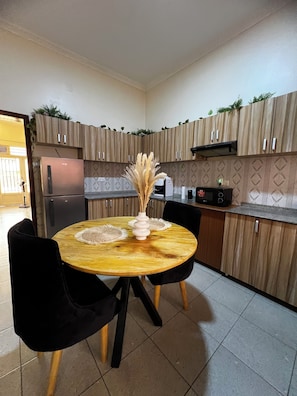 A compact kitchen with wooden cabinets, a built-in refrigerator, a round wooden table with two chairs, and a decorative vase with dried plants.