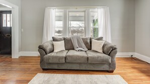 A grey sofa with white cushions in a room with wooden flooring, a white rug, and a window with white curtains. - 8 Mi to Micron Technology! Walkable Phoenix Gem (Phoenix)