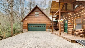 Eine Blockhütte mit einer grünen Garagentür, einem gepflasterten Auffahrt und einem Sitzbereich im Freien mit Korbstühlen.