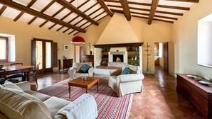 A spacious living room with a high ceiling, exposed wooden beams, a fireplace, and a dining area with a table and chairs. - Podere i Prati-Tuscan vacation house in the Val D'Orcia (Chianciano Terme)