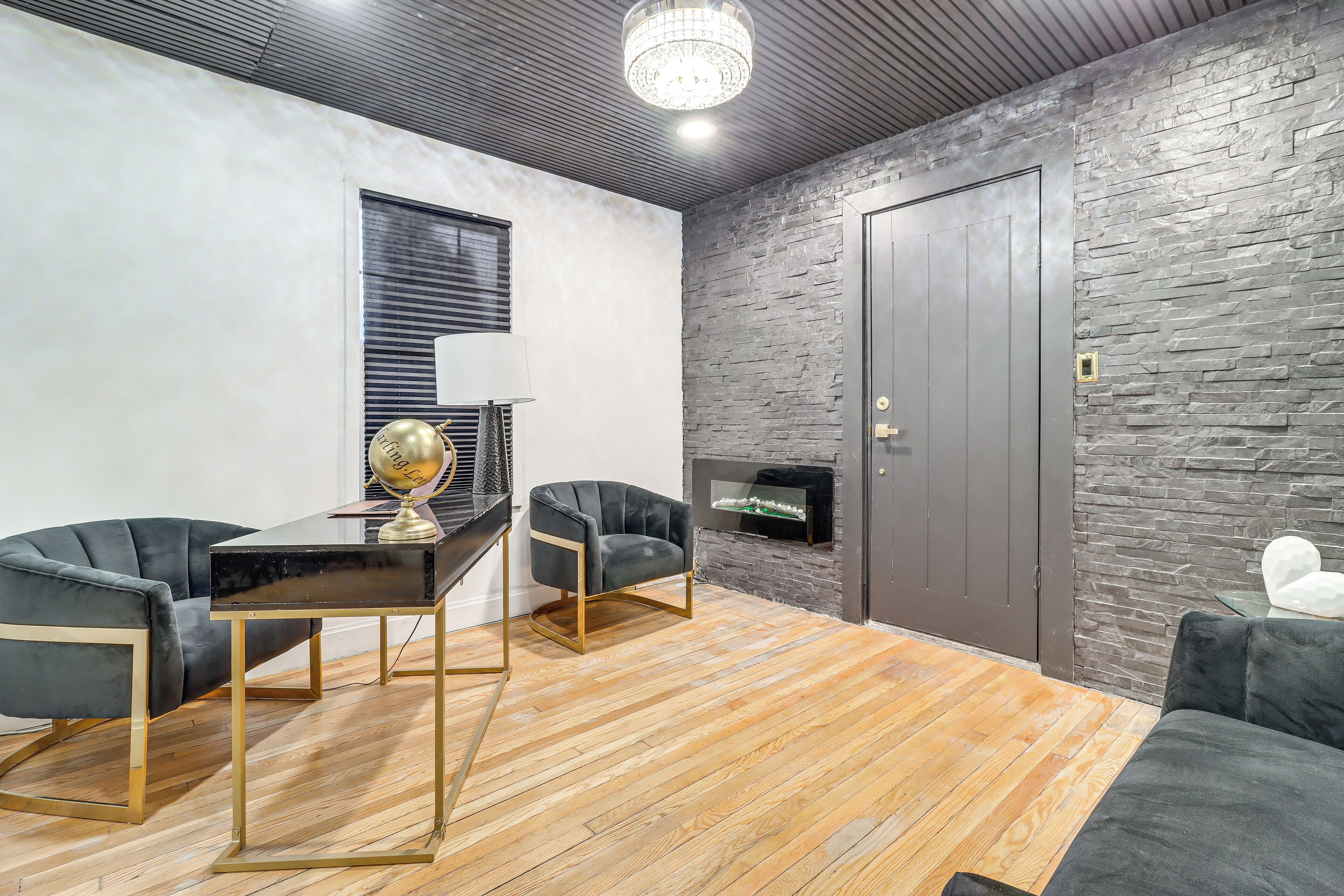 Uma sala de estar moderna com lareira, um sofá de couro preto, uma mesa preta com moldura dourada e piso de madeira.