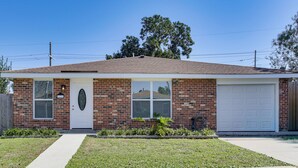 A single-story brick house with a white garage door, a front entrance with a door and window, and a small front yard with grass and plants.