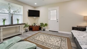 A bedroom with a bed, a desk, a television, a ceiling fan, and a window with blinds.