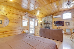 Ein Blockhaus-Zimmer mit einem Bett, einem Schlafsofa, einem Fernseher und einer Steinwand.