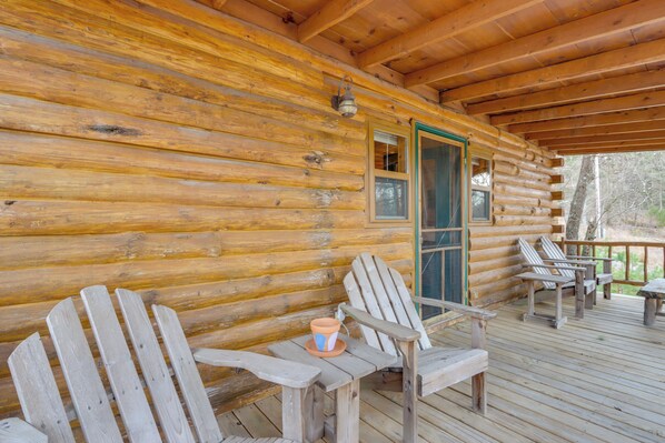 A wooden cabin with a porch, two Adirondack chairs, and a table with a potted plant. - Hike, Play On-Site: Eureka Springs Cabin Near Dtwn (Eureka Springs)