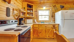 Cocina de cabaña de madera con estufa, microondas, refrigerador, armarios de madera y una ventana.